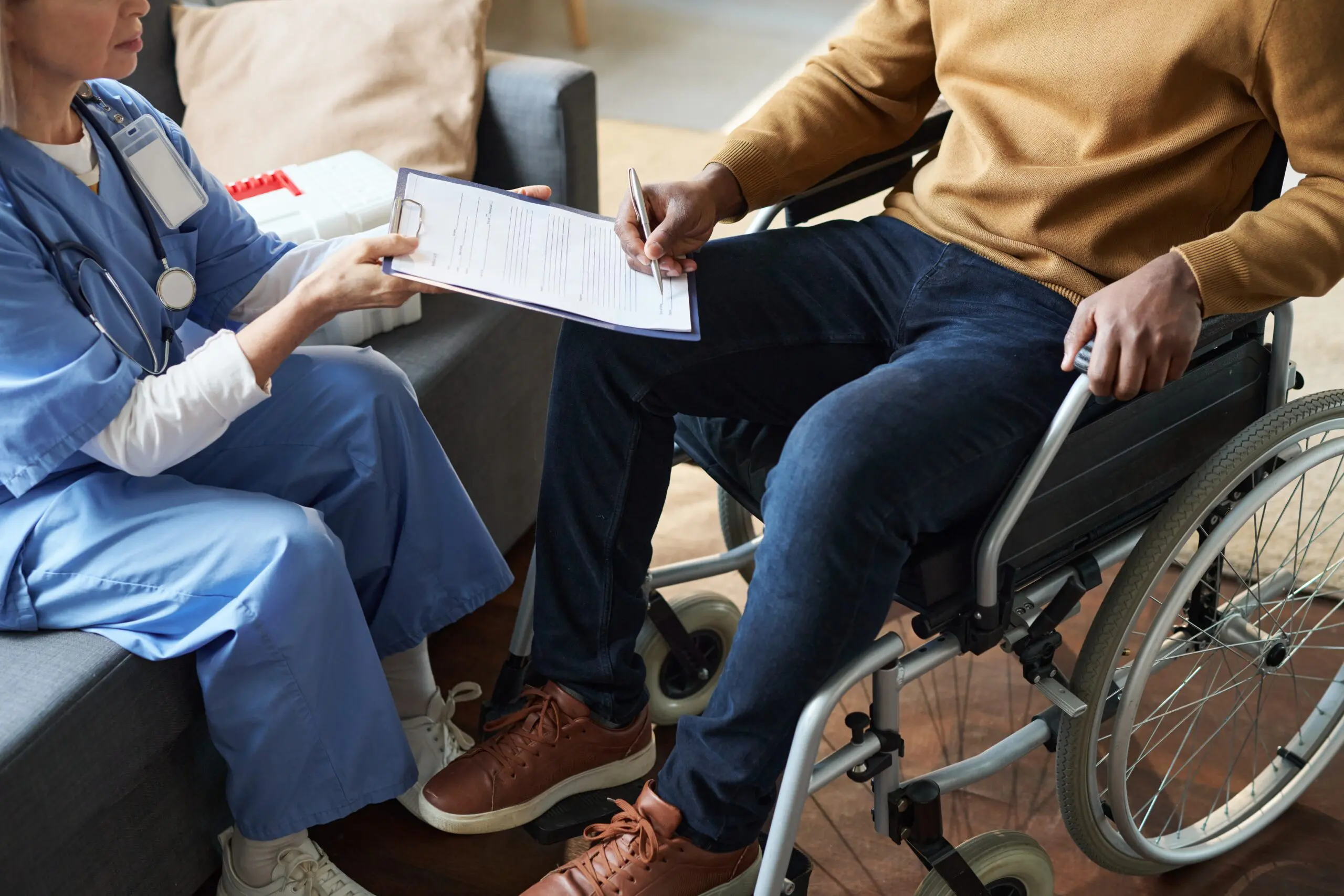 Cropped shot of African American man with disability using wheelchair and signing medical form during at home doctors visit copy space